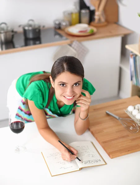 Gelukkig mooie vrouw permanent in haar keuken schrijven op een laptop thuis — Stockfoto