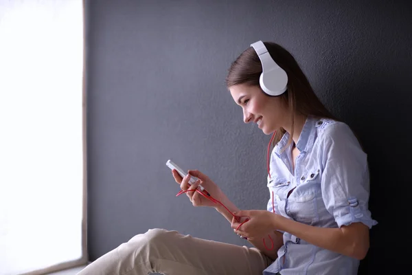 Smiling girl with headphones sitting on the floor near wall — Stock Photo, Image