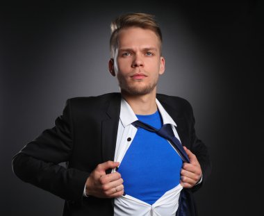 Genç işadamı hareket ve bir süper kahraman gibi gömleğini, yırtılma gri arka plan üzerinde izole