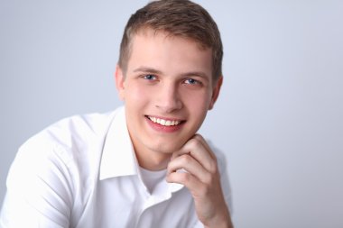 Gri arka plan üzerinde oturan gülümseyen genç adam portresi