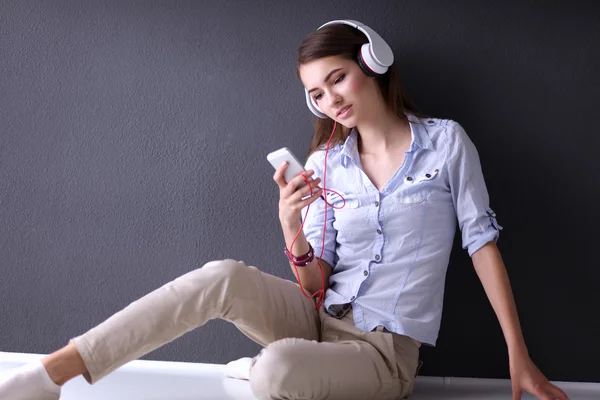 Smiling girl with headphones sitting on the floor near wall — Stock Photo, Image