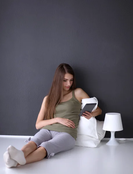 Mulher morena bonita sentada no chão com uma almofada e mesa plana — Fotografia de Stock