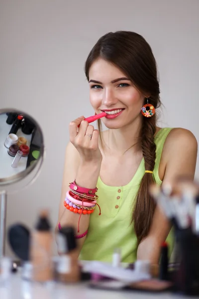 Młoda kobieta piękne Dokonywanie makijaż w pobliżu lustro, siedząc przy biurku — Zdjęcie stockowe