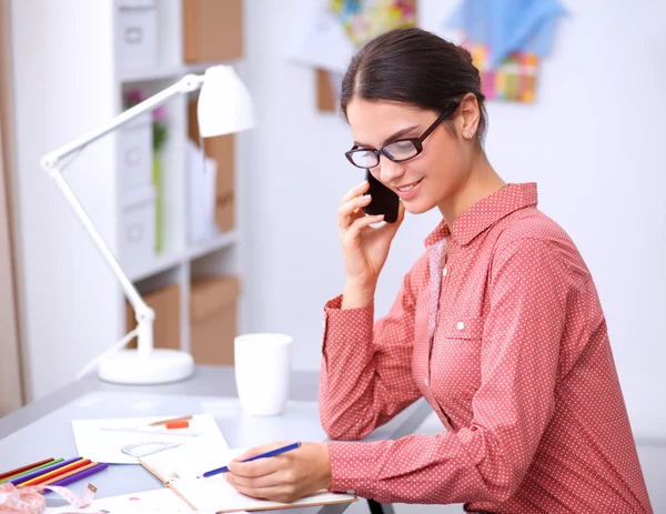 Jonge aantrekkelijke vrouwelijke mode-ontwerper werken op kantoor bureau, tekenen terwijl het praten op mobiele — Stockfoto