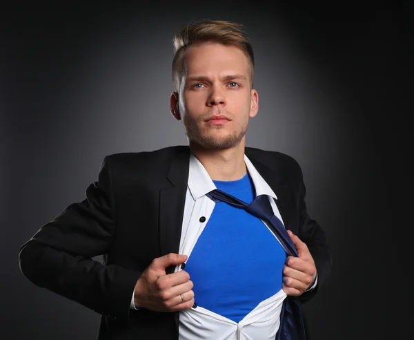 Joven hombre de negocios actuando como un súper héroe y rasgando su camisa, aislado sobre un fondo gris — Foto de Stock