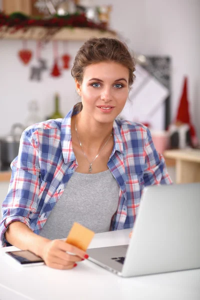 Mulher sorrindo compras on-line usando computador e cartão de crédito na cozinha — Fotografia de Stock