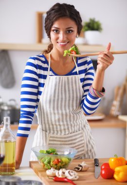 Genç kadın modern mutfakta taze salata yiyor.