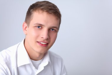 Gri arka plan üzerinde oturan gülümseyen genç adam portresi