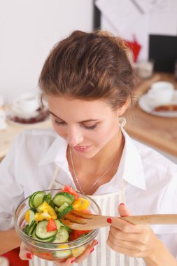 Genç kadın modern mutfakta taze salata yiyor.