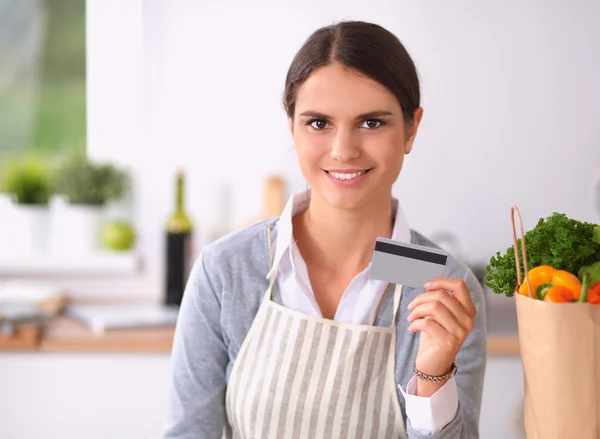 Mujer sonriente compras en línea utilizando la computadora y la tarjeta de crédito en la cocina — Foto de Stock