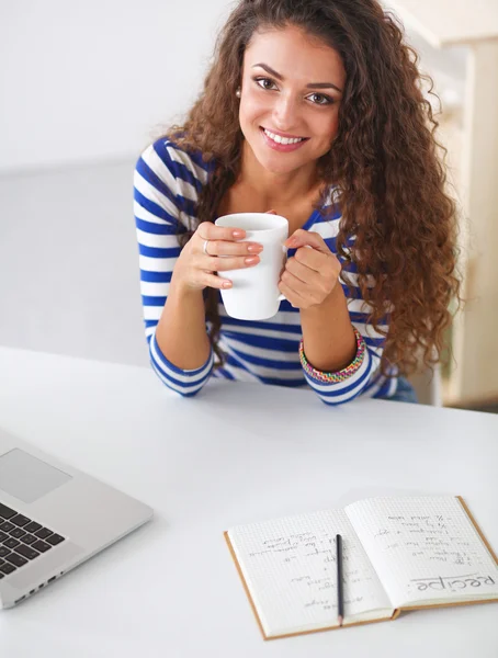 Sorrindo jovem com xícara de café e laptop na cozinha em casa — Fotografia de Stock