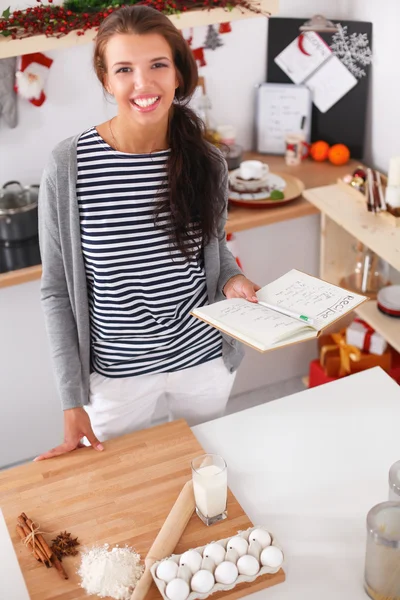 Glimlachende jonge vrouw in de keuken, geïsoleerd op kerst achtergrond — Stockfoto