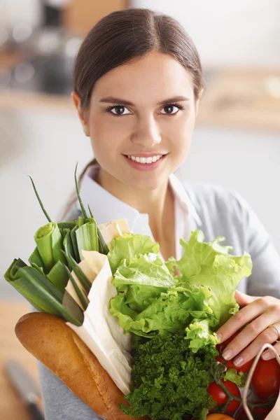 Mujer joven sosteniendo bolsa de la compra de comestibles con verduras de pie en la cocina. — Foto de Stock