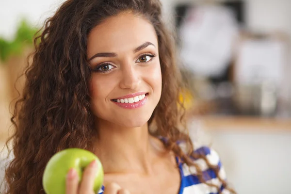 快乐的年轻女人在厨房里吃苹果 — 图库照片