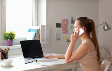 Genç iş kadını masada oturuyor ve telefonla konuşuyor.