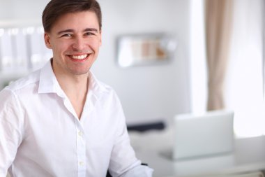 Genç işadamı ofiste çalışıyor, masada oturuyor.