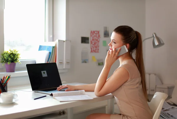 Jonge zakenvrouw zit aan het bureau en praat over de telefoon — Stockfoto