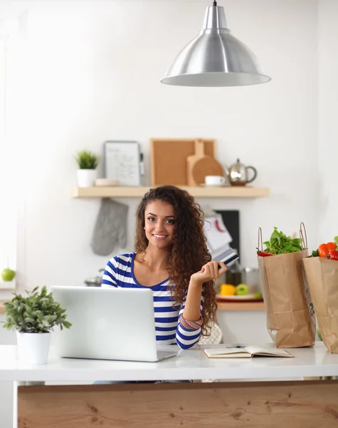 Mujer joven sonriente con taza de café y portátil en la cocina en casa — Foto de Stock