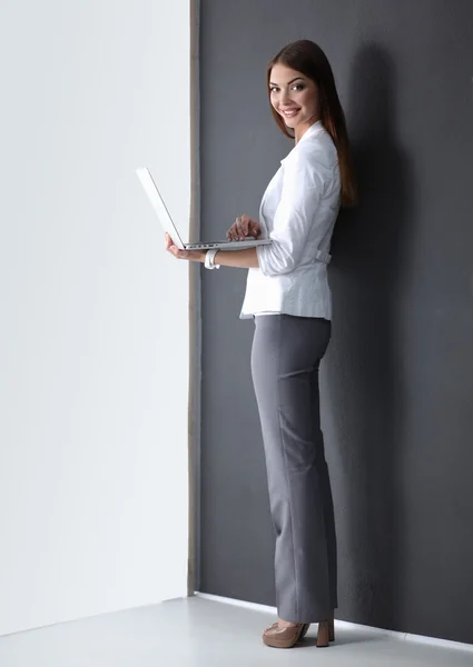 Jonge vrouw met een laptop, staande op een grijze achtergrond — Stockfoto