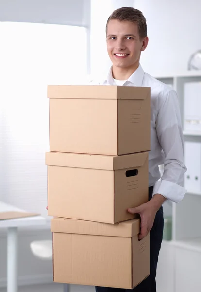 Young Man holding a stack of cardboard boxes standing in office — Stock Photo, Image