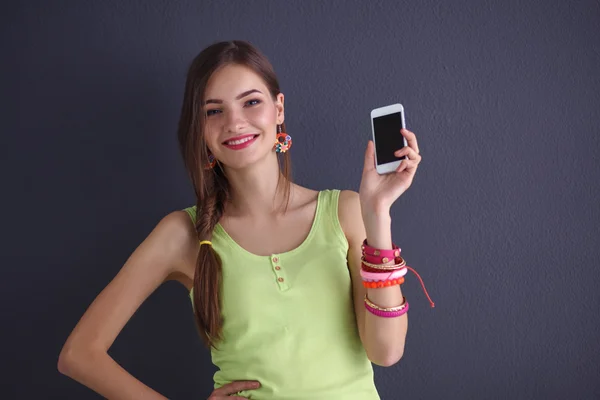 Hermosa mujer joven sosteniendo el teléfono celular, de pie cerca de la pared oscura — Foto de Stock