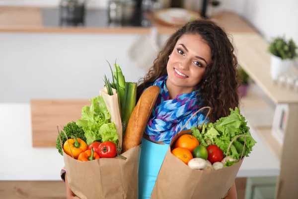 Jonge vrouw met boodschappentas met groenten Staande in de keuken. — Stockfoto