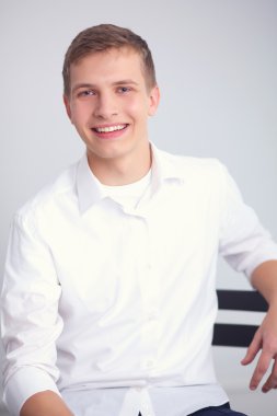 Gri arka plan üzerinde oturan gülümseyen genç adam portresi