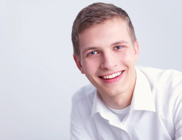 Retrato de un joven sonriendo sentado sobre un fondo gris —  Fotos de Stock