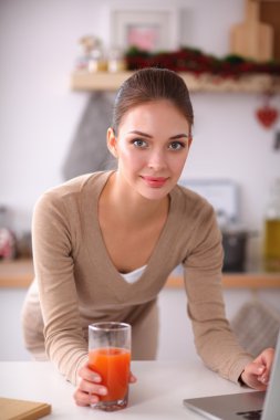 mutfağında suyu yudumlarken bir dizüstü bilgisayar kullanan kadın