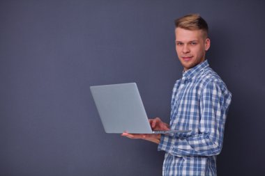 Gri arka plan üzerinde dizüstü bilgisayar konumu olan kendine güvenen genç adam portresi