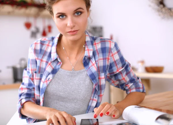 Mujer sonriente sosteniendo su teléfono celular en la cocina — Foto de Stock