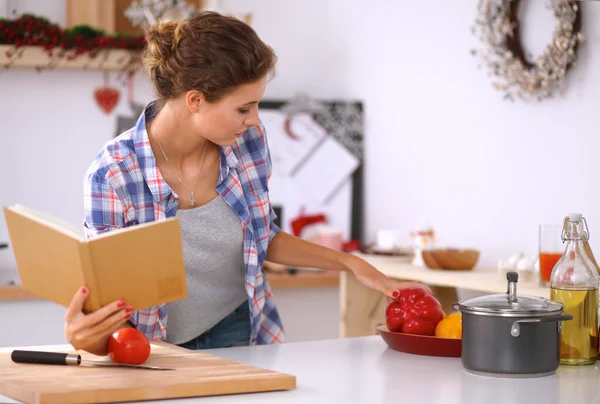 Ung kvinna läser kokbok i köket, letar efter recept — Stockfoto