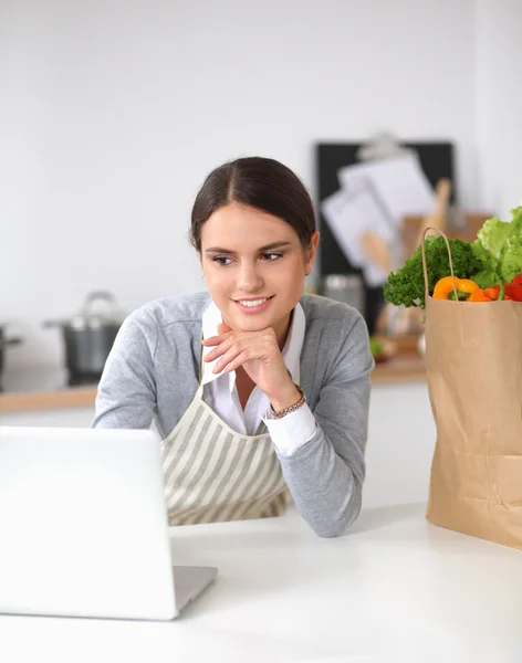 Hermosa joven cocina mirando a la pantalla del ordenador portátil con recibo en la cocina —  Fotos de Stock