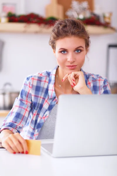 Mujer sonriente compras en línea utilizando la computadora y la tarjeta de crédito en la cocina — Foto de Stock