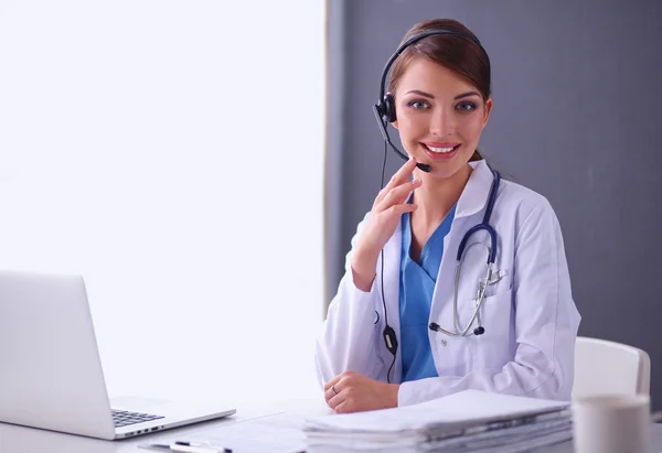 Médico con auriculares sentado detrás de un escritorio con portátil —  Fotos de Stock