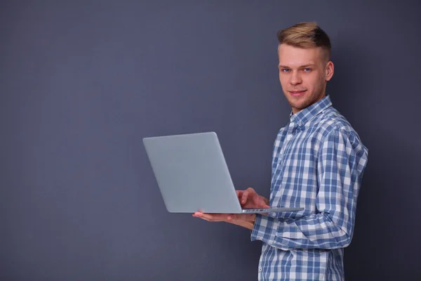 รูปภาพของชายหนุ่มที่มั่นใจกับแล็ปท็อป ยืนอยู่เหนือพื้นหลังสีเทา — ภาพถ่ายสต็อก
