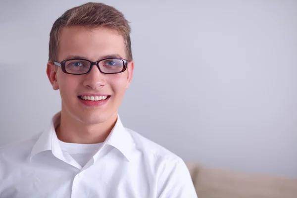 Портрет молодого человека, улыбающегося сидя на сером фоне — стоковое фото
