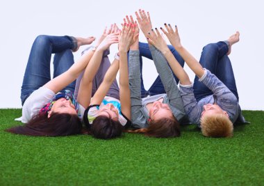 Yeşil çimenlerin üzerinde elleriyle yalan dört genç kadın