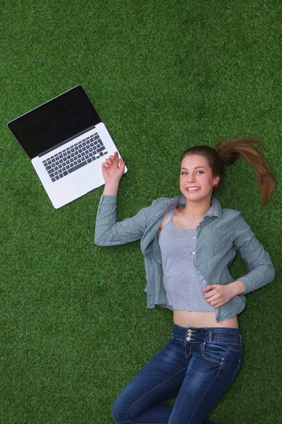 Relajada mujer acostada en la hierba cerca de la computadora portátil —  Fotos de Stock