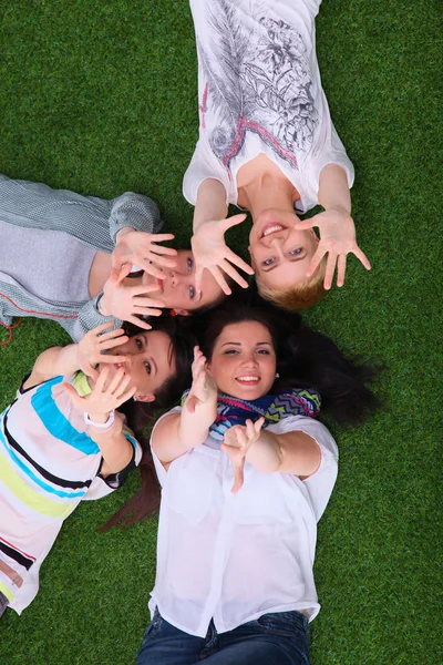 Quatro mulheres jovens deitadas na grama verde com as mãos para cima — Fotografia de Stock