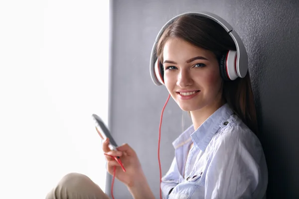 Lächelndes Mädchen mit Kopfhörern, das auf dem Boden neben der Wand sitzt — Stockfoto