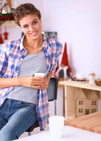 Mujer sonriente sosteniendo su teléfono celular en la cocina — Foto de Stock