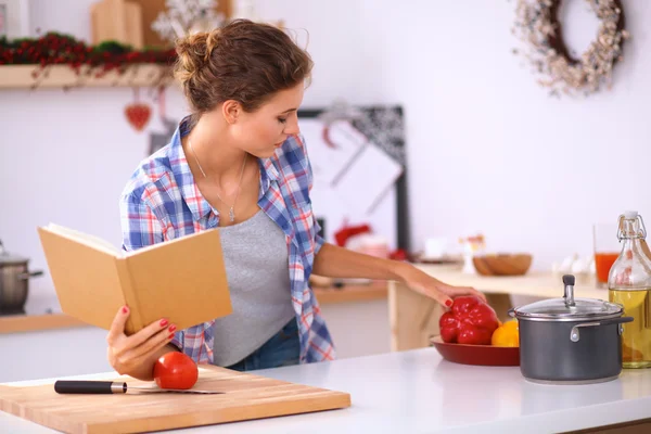 Mujer joven leyendo libro de cocina en la cocina, buscando receta — Foto de Stock