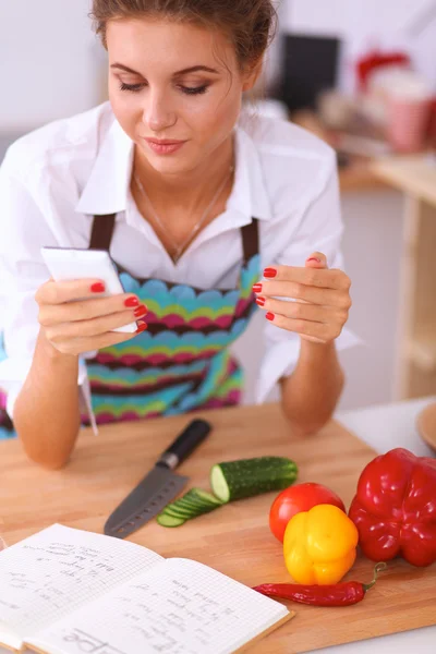 Leende kvinna som håller sin mobil i köket — Stockfoto