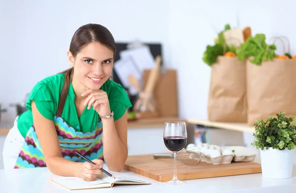 Gelukkig mooie vrouw permanent in haar keuken schrijven op een laptop thuis — Stockfoto