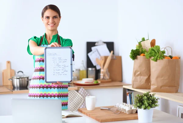 Kvinna i köket hemma, stående nära skrivbord med mapp — Stockfoto