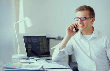 Genç işadamı ofiste çalışıyor, masada oturuyor.