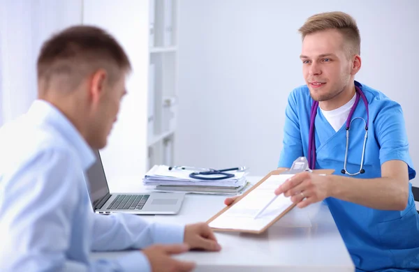 Portret van een lachende mannelijke arts met laptop aan het bureau in medisch kantoor — Stockfoto