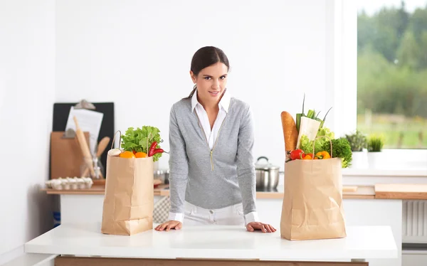 Mujer con bolsas de compras en la cocina en casa, de pie cerca del escritorio —  Fotos de Stock