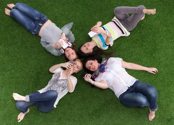 Τέσσερις νέες γυναίκες που βρίσκεται στο πράσινο γρασίδι με κινητό τηλέφωνο — Φωτογραφία Αρχείου